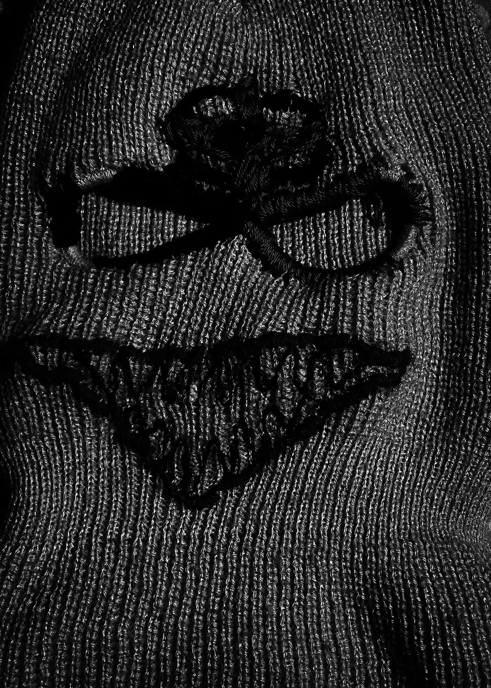 Cagoule nº 1 à plat en noir et blanc : relief des broderies sur la maille côtelée