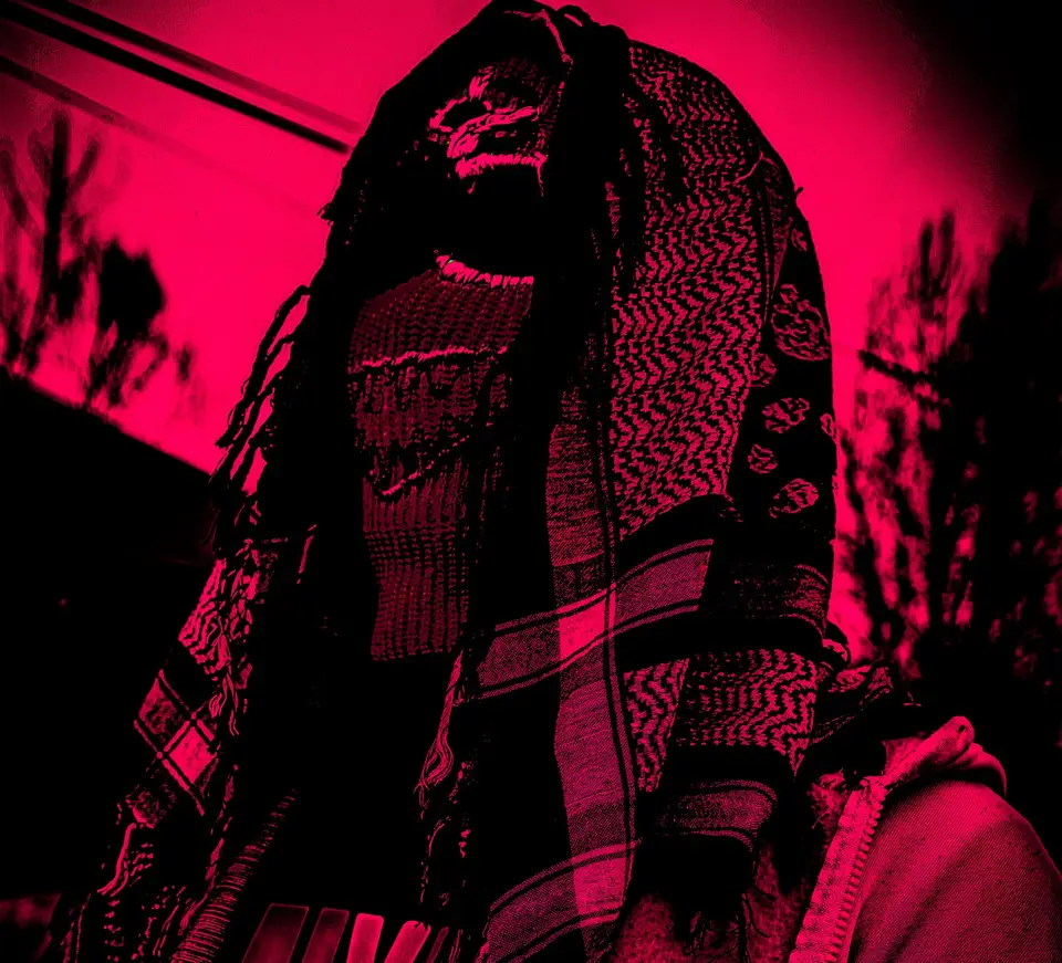 Silhouette sous un keffieh portant une cagoule brodée, lumière rose